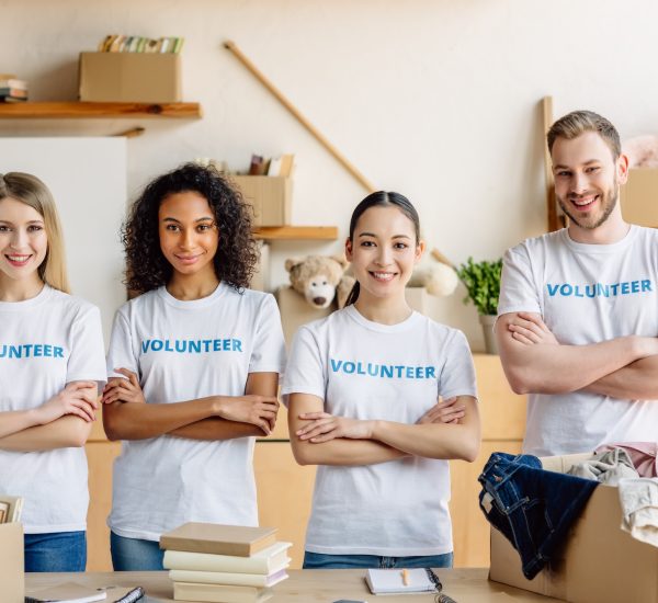 four-smiling-young-volunteers-in-white-t-shirts-with-volunteer-inscriptions-smiling-and-looking-at.jpg